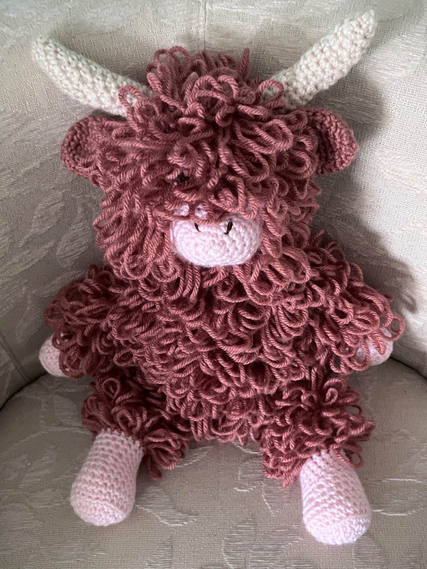 Gus crochet highland coo A fluffy, russet and pink crochet toy cow with curly fur and horns.